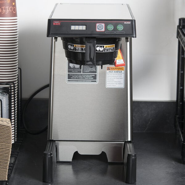 A Bunn SmartWAVE airpot coffee brewer on a counter next to a coffee cup.
