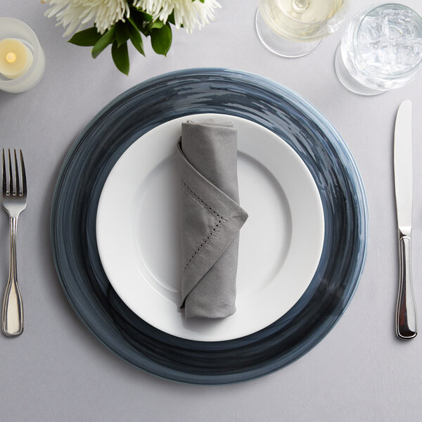 A black Alabaster glass charger plate on a table set with silverware and a napkin.
