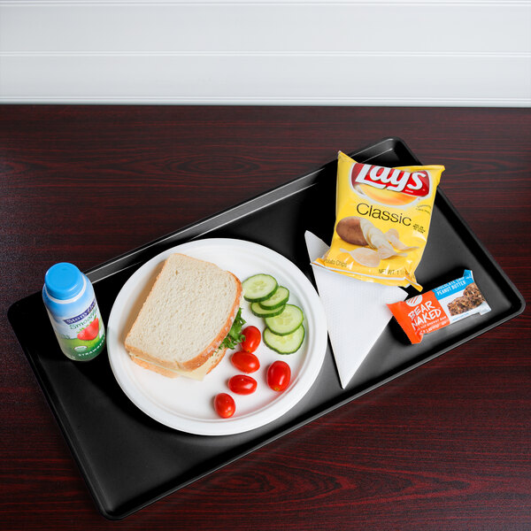 A black Cambro dietary tray with a sandwich, chips, and a blue drink bottle on it.