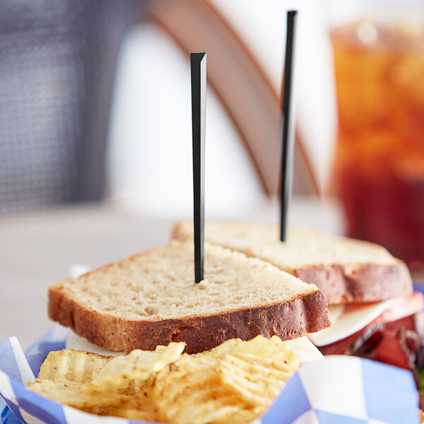 A sandwich with a black plastic prism food pick in it, with chips and a drink on the side.