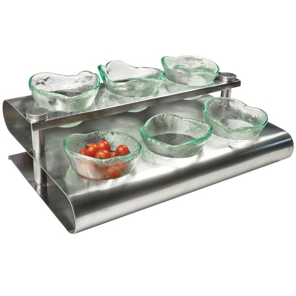 A Clipper Mill stainless steel S-shaped condiment rack holding glass bowls of tomatoes on a metal shelf.