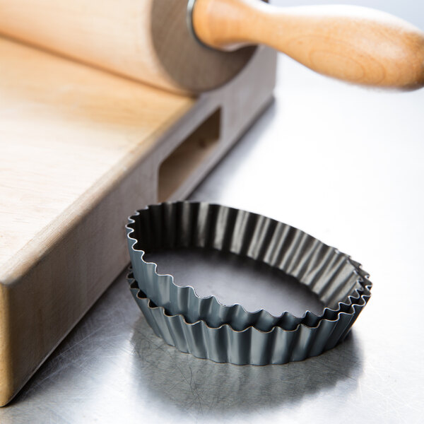 A Matfer Bourgeat fluted metal tartlet mold on a wooden surface.