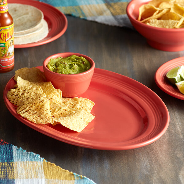 A Tuxton Cinnebar oval china platter with a bowl of chips and salsa on a table.