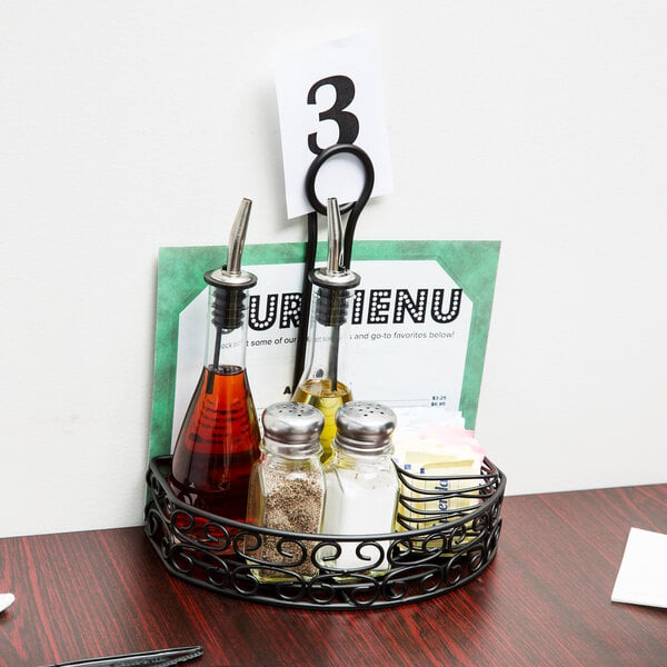 A black wrought iron half round condiment caddy with a card holder on a table with condiments and a menu.