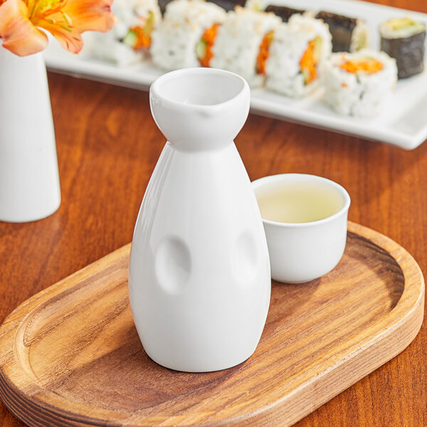 A close-up of a white Acopa sake bottle and cup on a wooden tray.