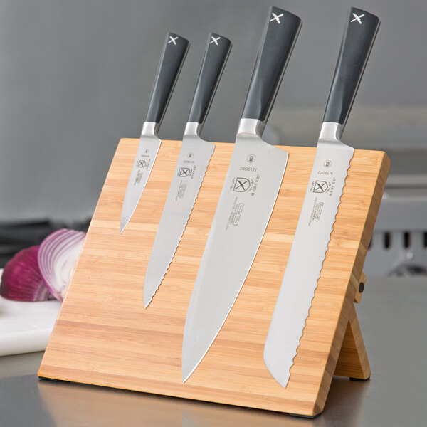 A group of Mercer Culinary knives on a bamboo magnetic board.