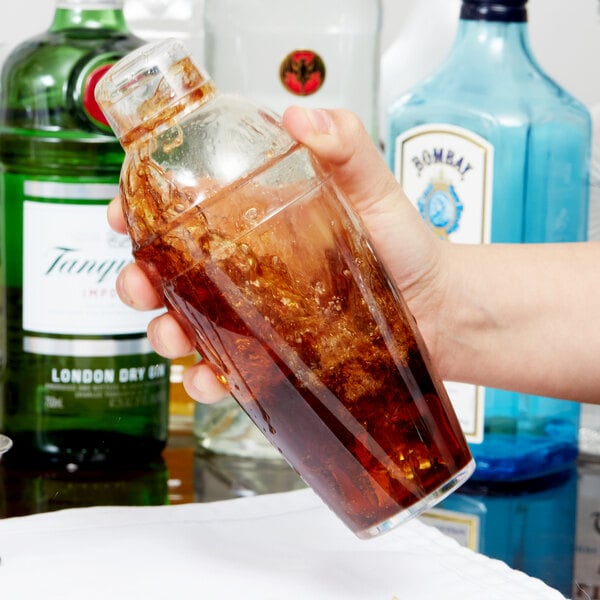 A hand holding a bottle of brown liquid over a glass with a brown liquid in it.