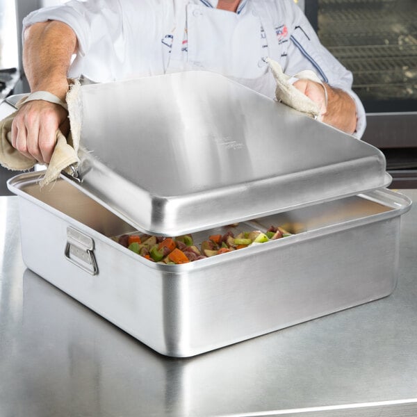 A chef using a Vollrath aluminum roasting pan to prepare food on a table.