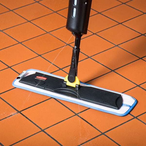 A Rubbermaid Light Commercial spray mop with a yellow handle cleaning a tile floor.