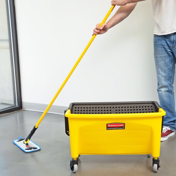 A man using a Rubbermaid HYGEN microfiber wet mop to clean a floor in a yellow and black container.