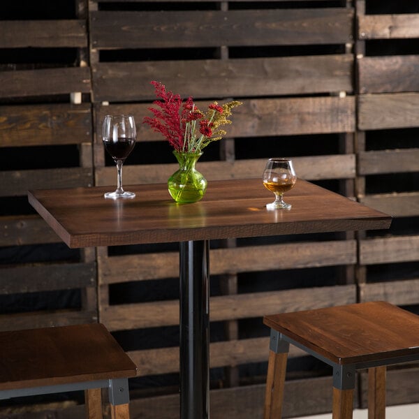 A Lancaster Table & Seating live edge table with wine glasses and a green vase of liquid on it.