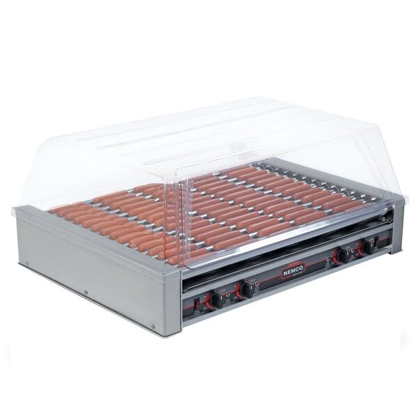 A Nemco hot dog roller grill with a clear cover filled with hot dogs.