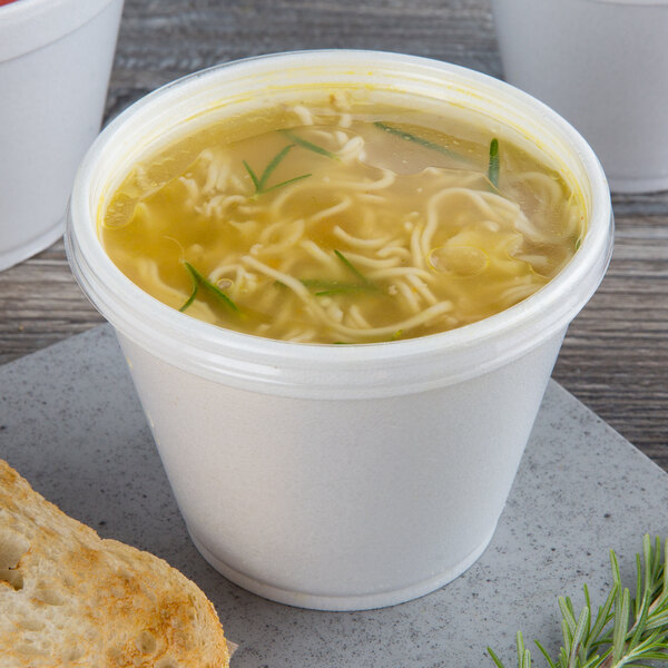 A clear Dart foam cup of soup with noodles and green onions.