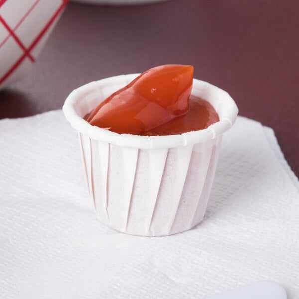 A Solo white paper portion cup filled with red food on a napkin.