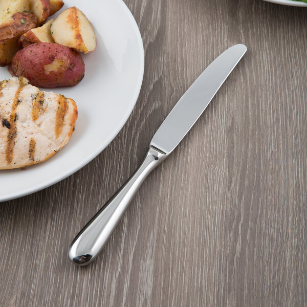 A Libbey stainless steel fluted hollow handle dinner knife on a plate of food.
