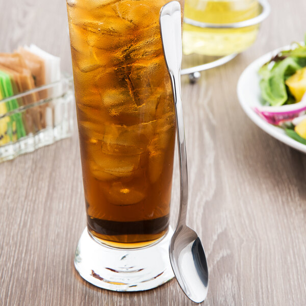 A glass of iced tea with a World Tableware stainless steel iced tea spoon on the table next to a bowl of salad.