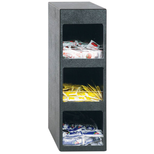 A black Vollrath 3-tier condiment organizer on a shelf with white and yellow condiment packets.