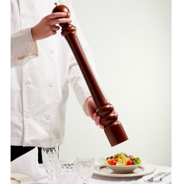 A chef using a Chef Specialties walnut pepper mill to grind pepper over a plate of salad.