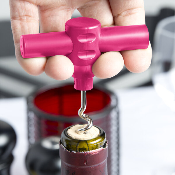 A hand holding a pink Franmara plastic pocket corkscrew opening a bottle of wine.