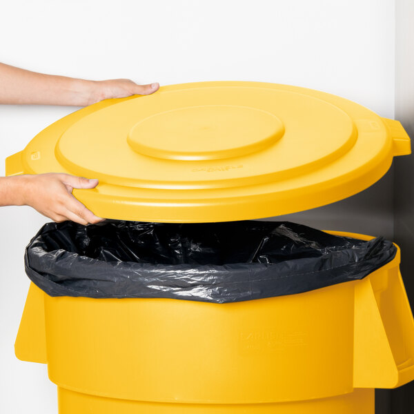 A hand placing a yellow lid on a Carlisle yellow trash can