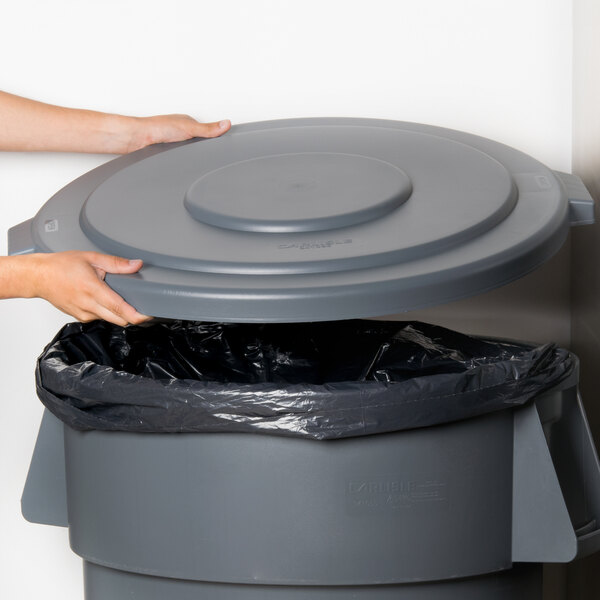 A person's hand opening a Carlisle gray flat round trash can lid.