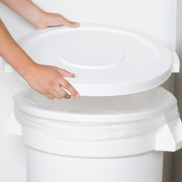 A hand reaching for a lid on a white Carlisle round trash can.