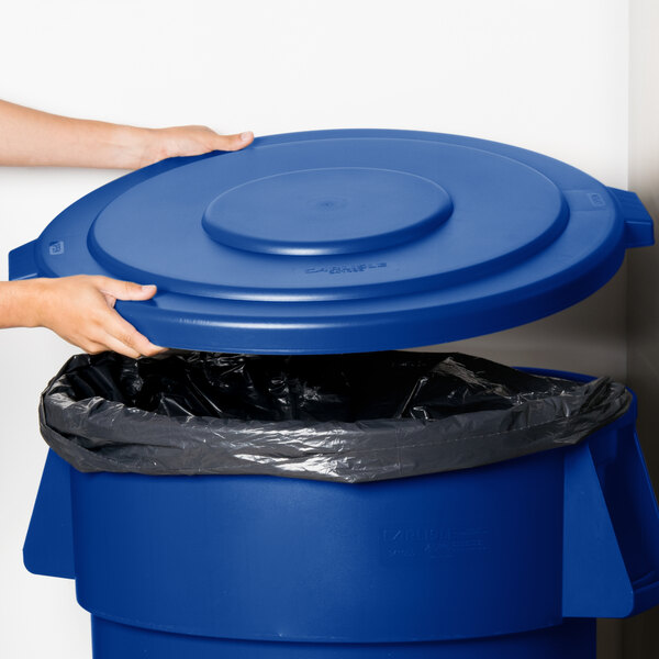 A person's hand holding a blue Carlisle Bronco trash can lid.