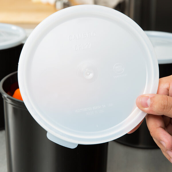 A hand holding a white Cambro plastic lid.