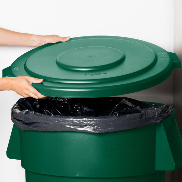 A hand placing a green Carlisle Bronco lid on a green trash can.