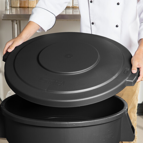 A person holding a Carlisle black round trash can lid.