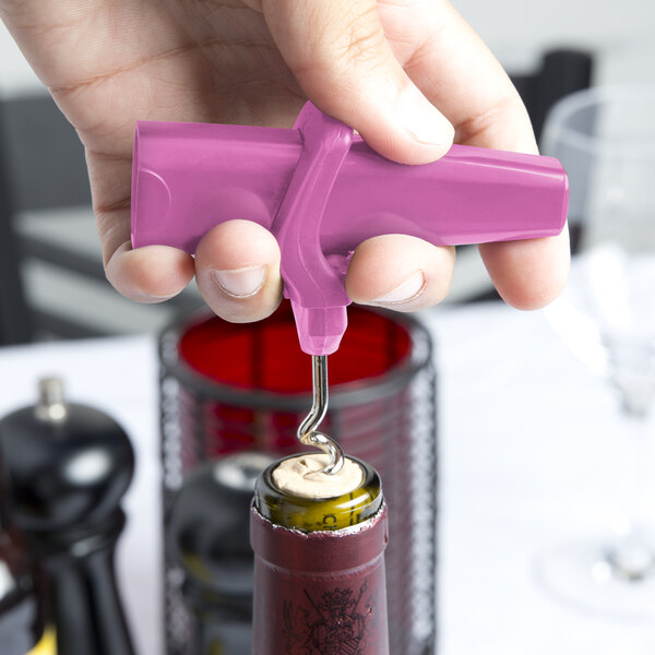 A person using a Franmara baby pink plastic corkscrew to open a wine bottle.