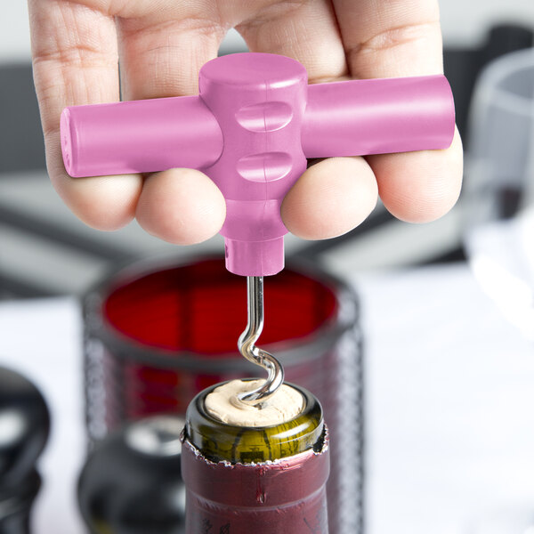 A hand holding a Franmara Baby Pink plastic corkscrew opening a wine bottle.