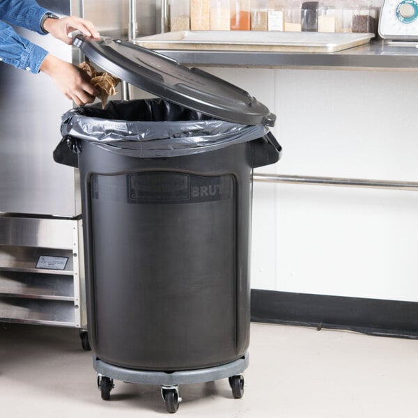 A woman opens a black Rubbermaid BRUTE trash can.