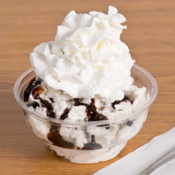 A Fabri-Kal clear plastic sundae cup filled with ice cream, whipped cream, and chocolate syrup.