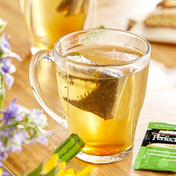 A glass mug of Bigelow Perfectly Mint tea with a tea bag in it.