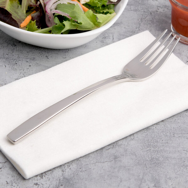 A Chef & Sommelier stainless steel salad fork on a napkin next to a bowl of salad.