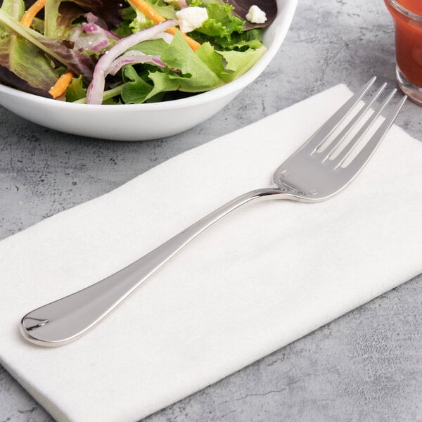 A Chef & Sommelier stainless steel salad fork on a napkin next to a bowl of salad.