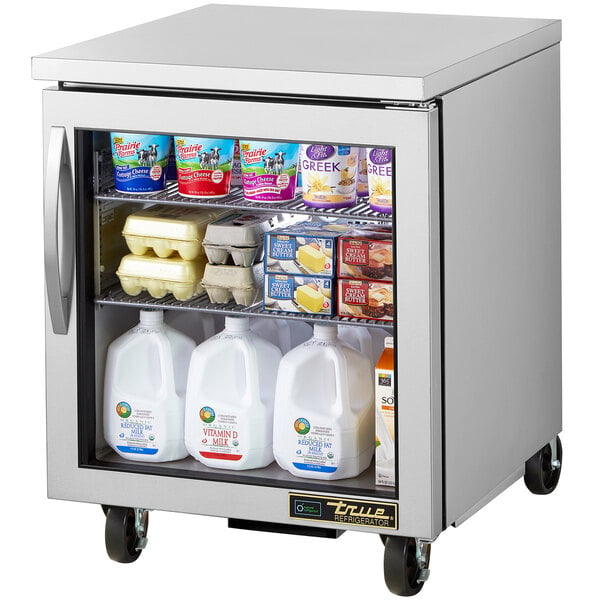 A True undercounter refrigerator with a glass door full of dairy products, including a white jug of milk.