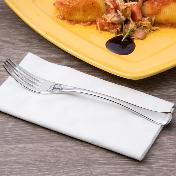 A silver Chef & Sommelier stainless steel dinner fork on a napkin next to a plate of pasta.