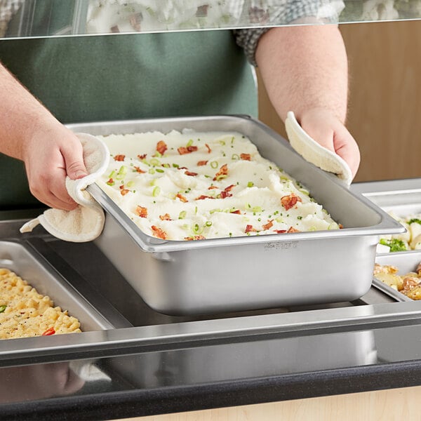 A person preparing food in a Hatco stainless steel food pan on a countertop.