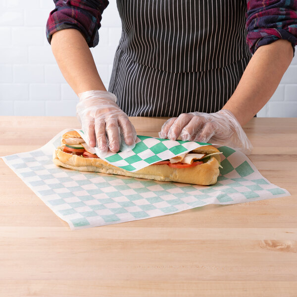 A person in gloves holding a sandwich with green and white Choice deli wrap