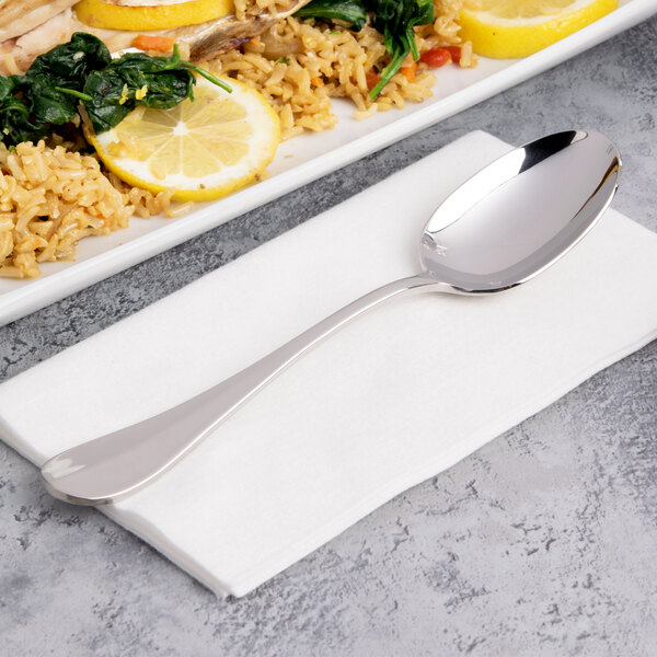 A Chef & Sommelier stainless steel dinner spoon on a napkin next to a plate of food.