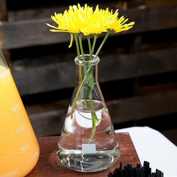 An American Metalcraft Erlenmeyer flask with yellow flowers on a table.