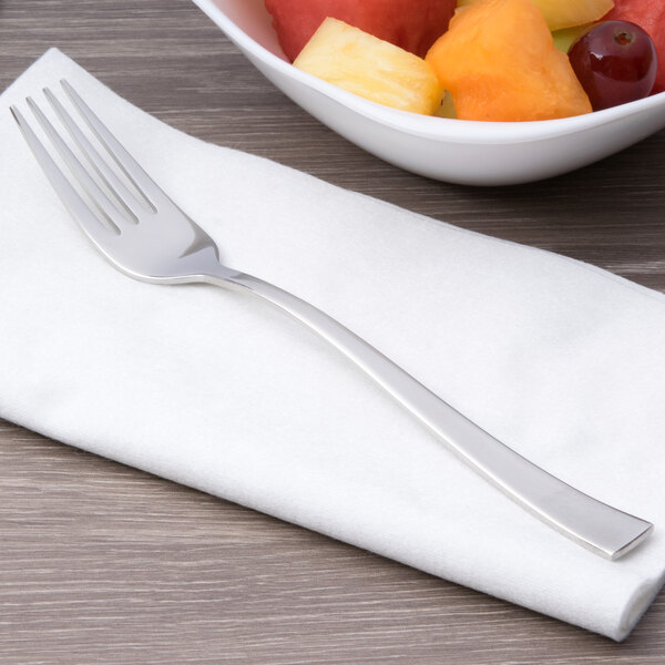 An Arcoroc stainless steel dessert fork on a napkin next to a bowl of fruit.