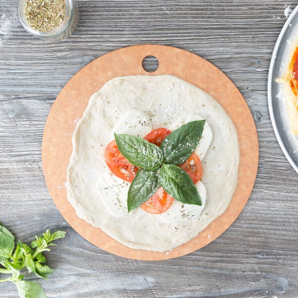 A pizza with tomatoes and basil on an Epicurean round wood pizza board.