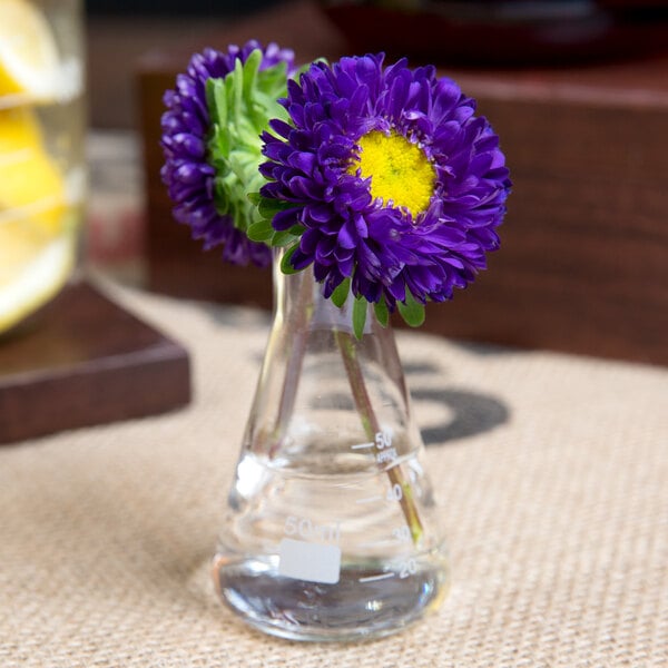 An American Metalcraft Erlenmeyer flask with purple and yellow flowers in it.