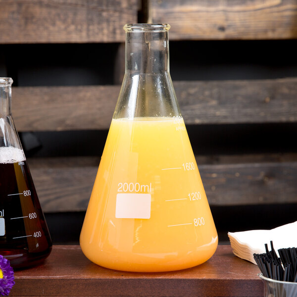 An American Metalcraft glass Erlenmeyer flask with yellow liquid inside on a table.