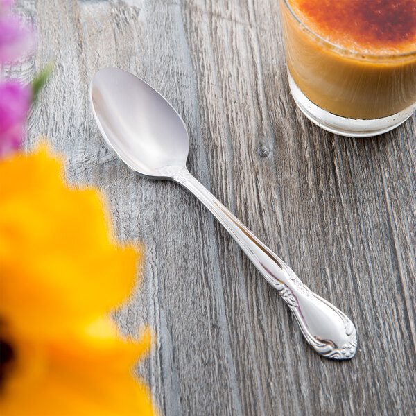 A Libbey Lady Astor stainless steel teaspoon next to a glass of orange juice on a table.