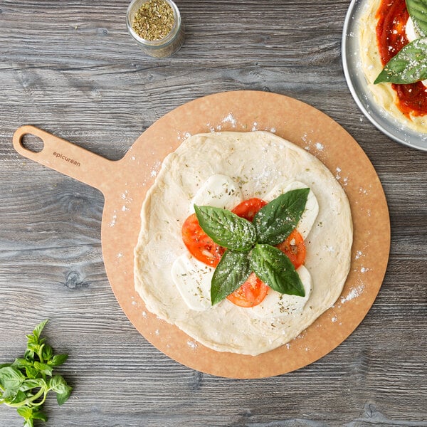 An Epicurean round pizza board with a pizza topped with tomatoes and basil.