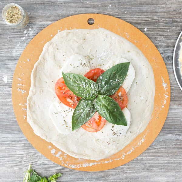 An Epicurean natural wood fiber pizza board with pizza dough, tomatoes and basil on top.